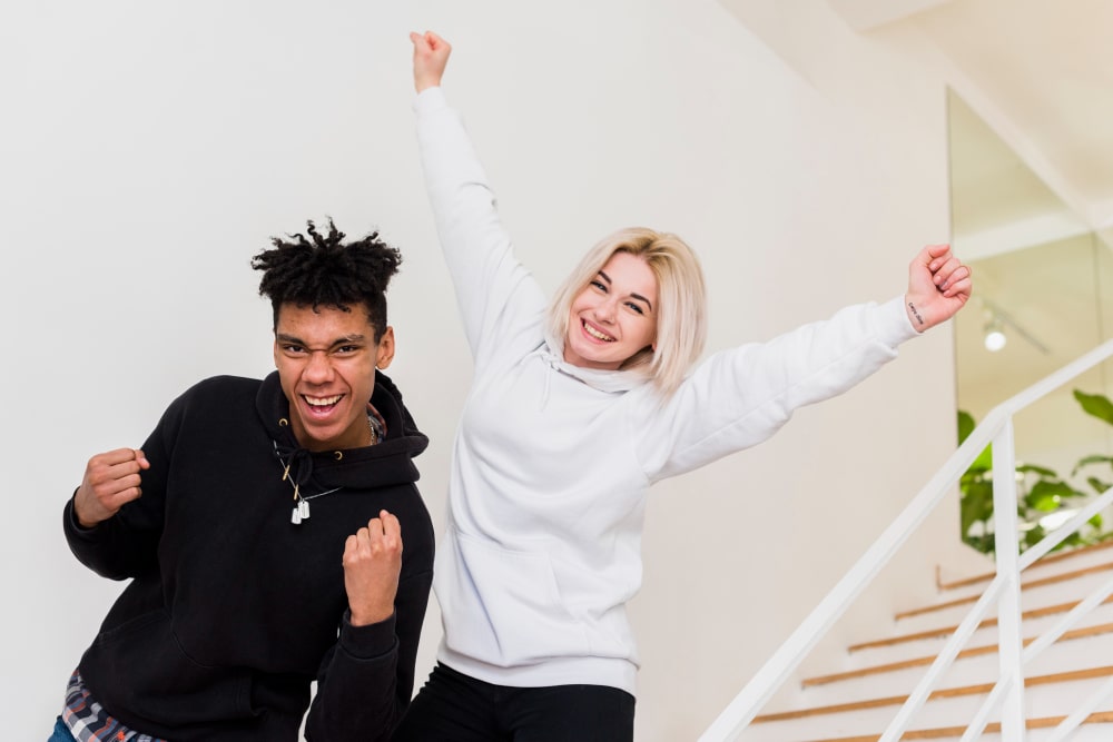 Joyful teenage interracial couple celebrating their success with excitement and happiness, surrounded by life changing motivational quotes.