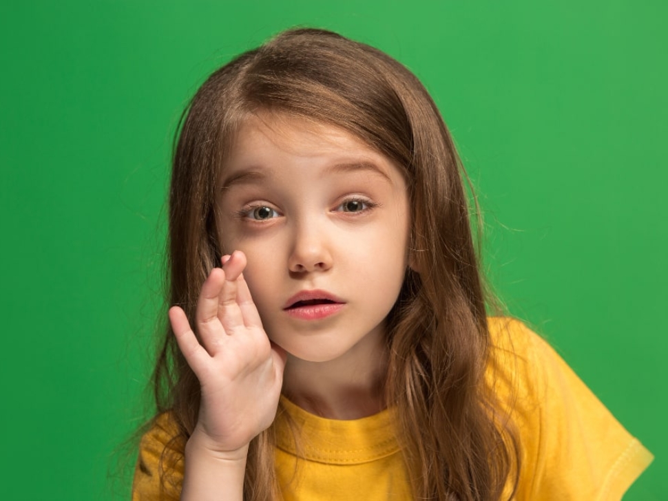 Image of a young teen girl whispering a secret behind her hand over a green background, symbolizing the concept of 'Leaked Secrets' and clandestine communication.