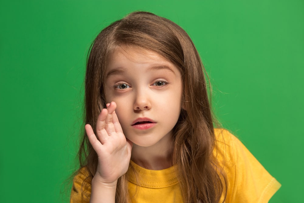 Image of a young teen girl whispering a secret behind her hand over a green background, symbolizing the concept of 'Leaked Secrets' and clandestine communication.